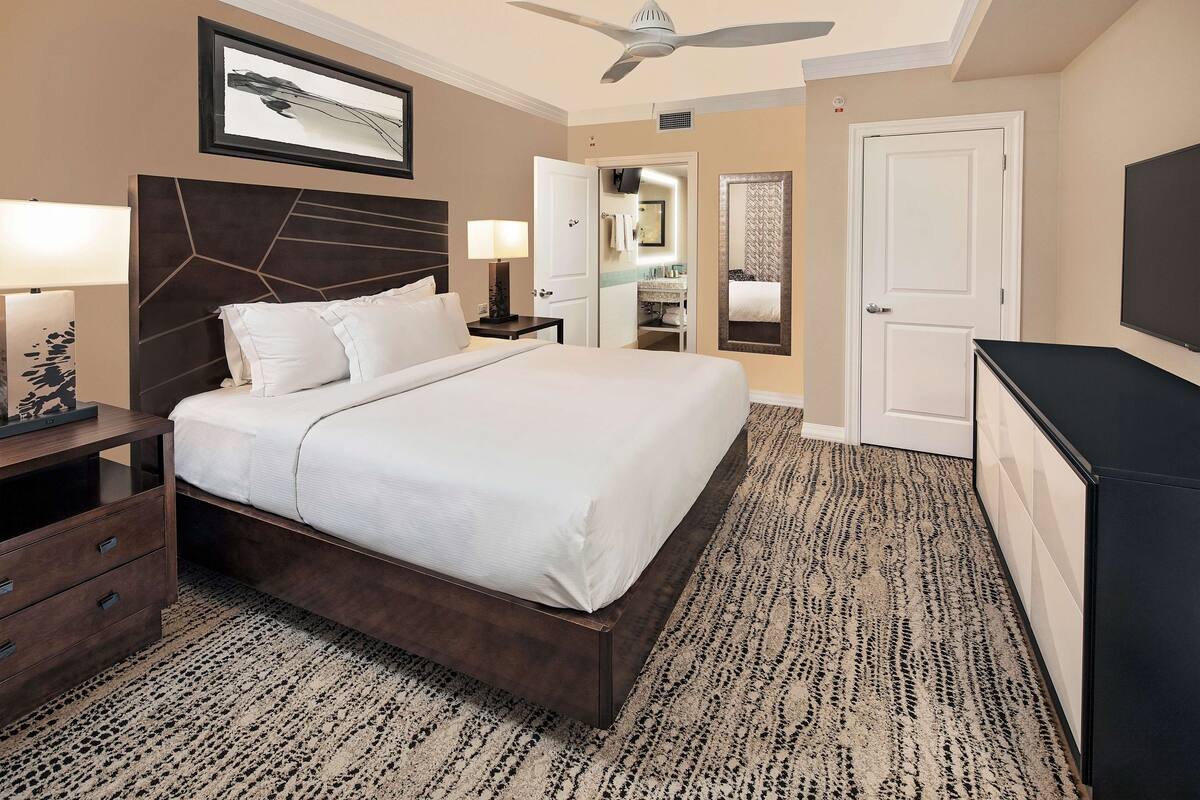 Ein Hotelzimmer mit einem großen Bett, einem Deckenventilator, einem Kleiderschrank, einem Schreibtisch und einem durch eine geöffnete Tür einsehbaren Badezimmer.