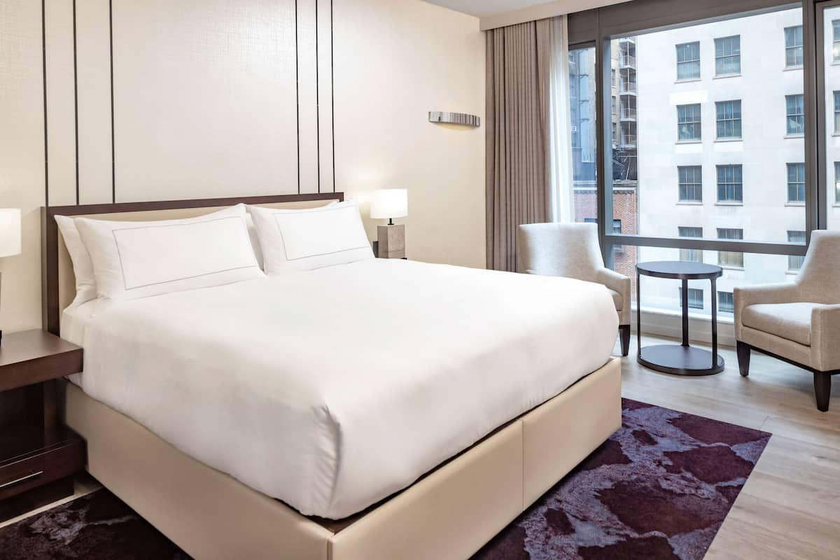 A hotel room with a large bed, two bedside lamps, a small round table, and a chair.