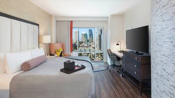 A hotel room with a large bed, a desk, a television, and a view of the cityscape.