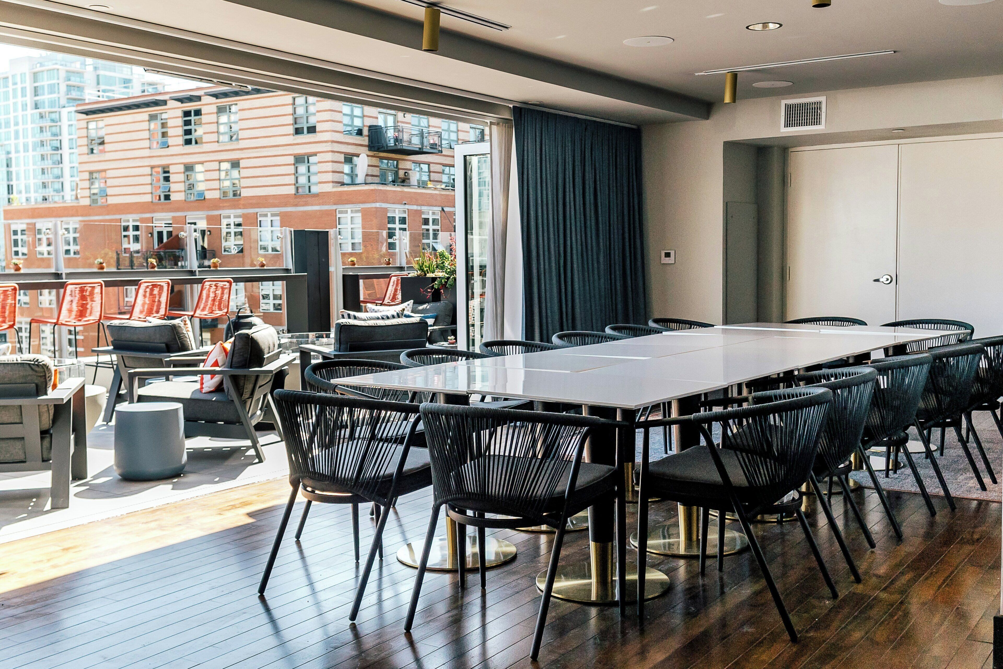 A modern conference room with a large table and chairs, large windows with a city view, and a balcony with outdoor seating.