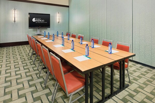 A conference room with a long table, chairs, water bottles, and a TV screen displaying the hotel name.