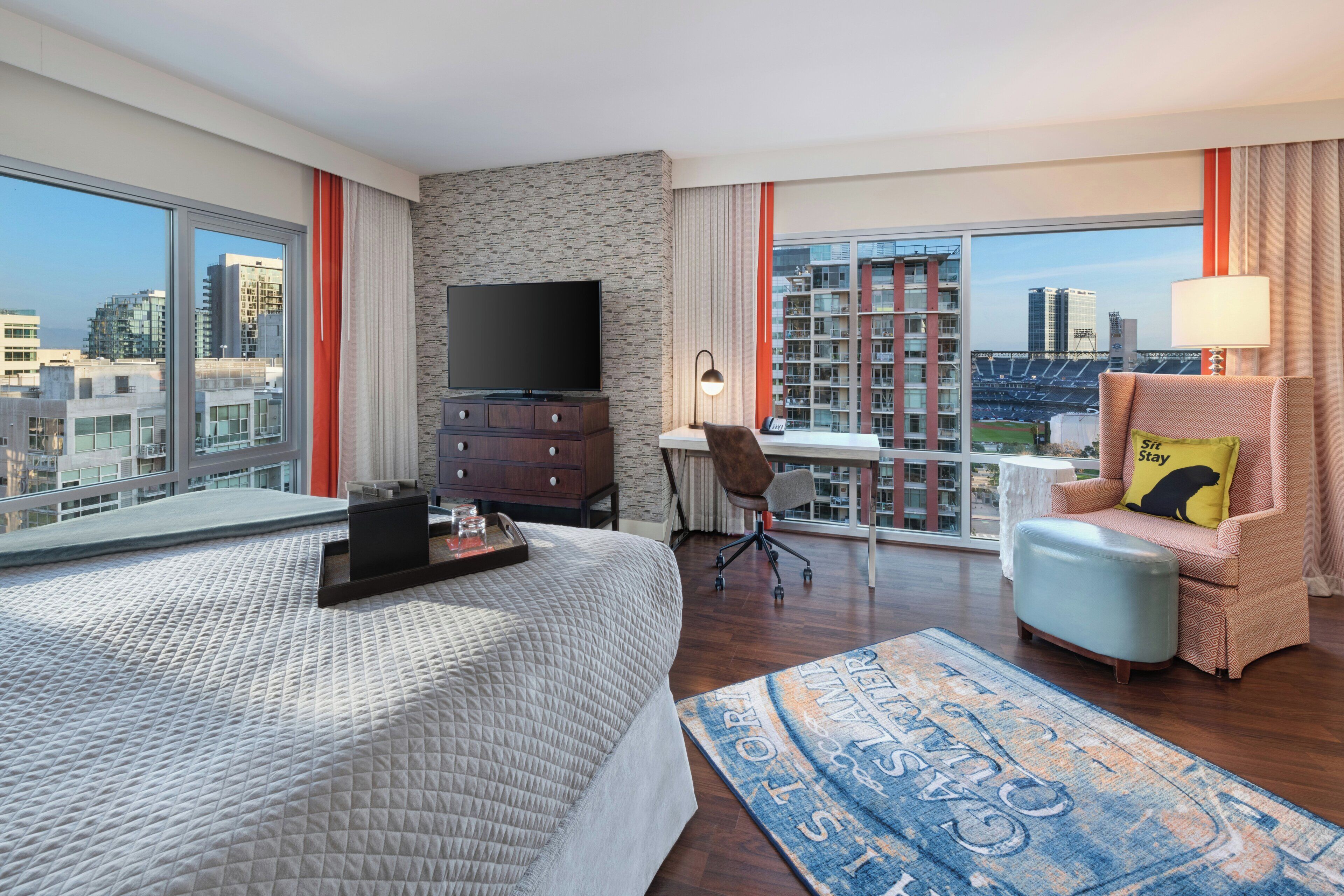 Een hotelkamer met een bed, een televisie, een bureau, een stoel en uitzicht op de stad.