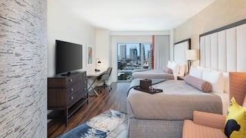 Ein Hotelzimmer mit einem großen Bett, einem Schreibtisch, einem Fernseher und Blick auf die Stadt.