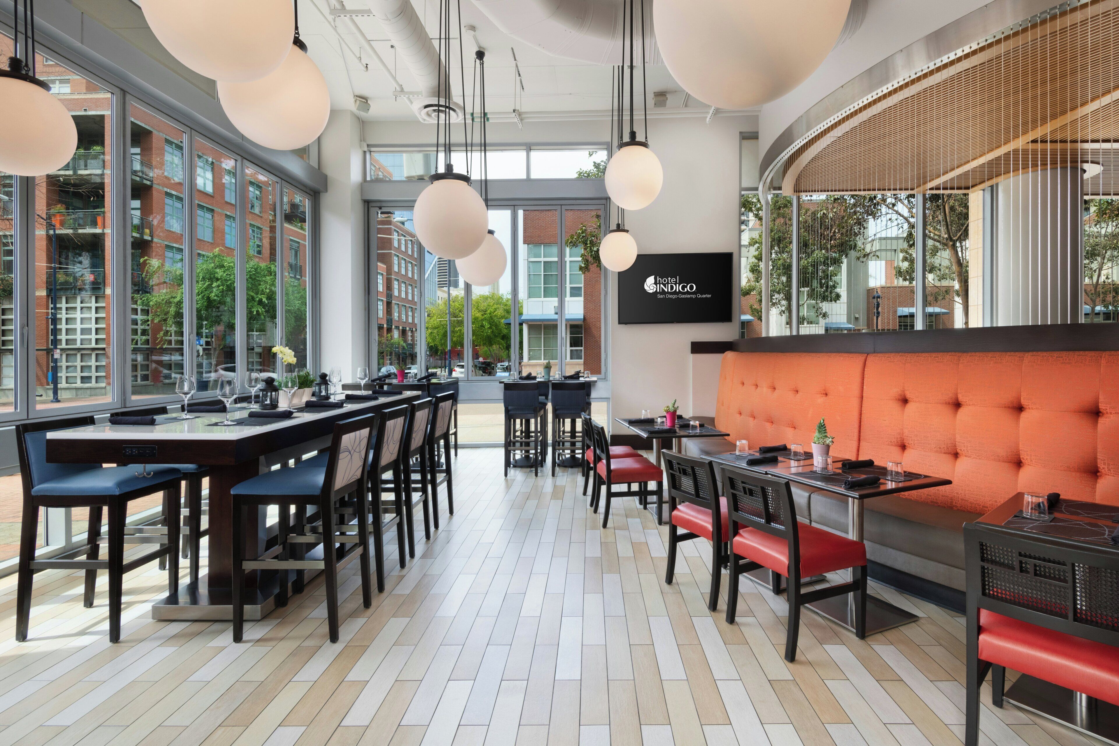 A modern restaurant interior with high ceilings, pendant lighting, and a mix of dining tables and booths.