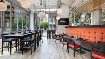 A modern restaurant interior with high ceilings, pendant lighting, and a mix of dining tables and booths.