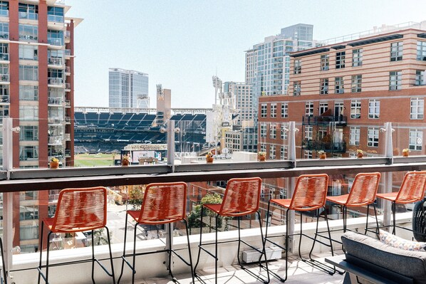 Un balcon avec des chaises orange et une vue sur un stade et les bâtiments de la ville.