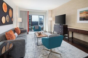 Een moderne woonkamer met een bank, fauteuils, een salontafel, een televisie en uitzicht op een stadion door een groot raam.