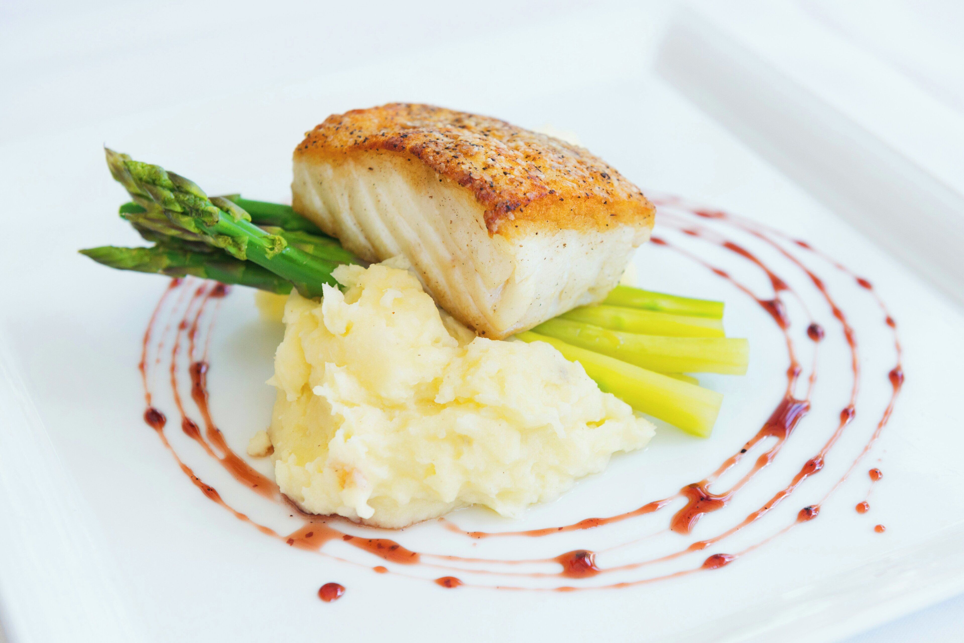 A plate with a piece of fish, asparagus, and mashed potatoes.
