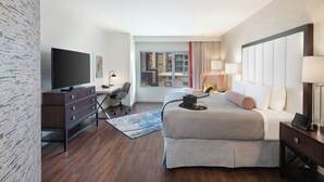 A hotel room with a bed, a desk, a television, and a view of the outside.