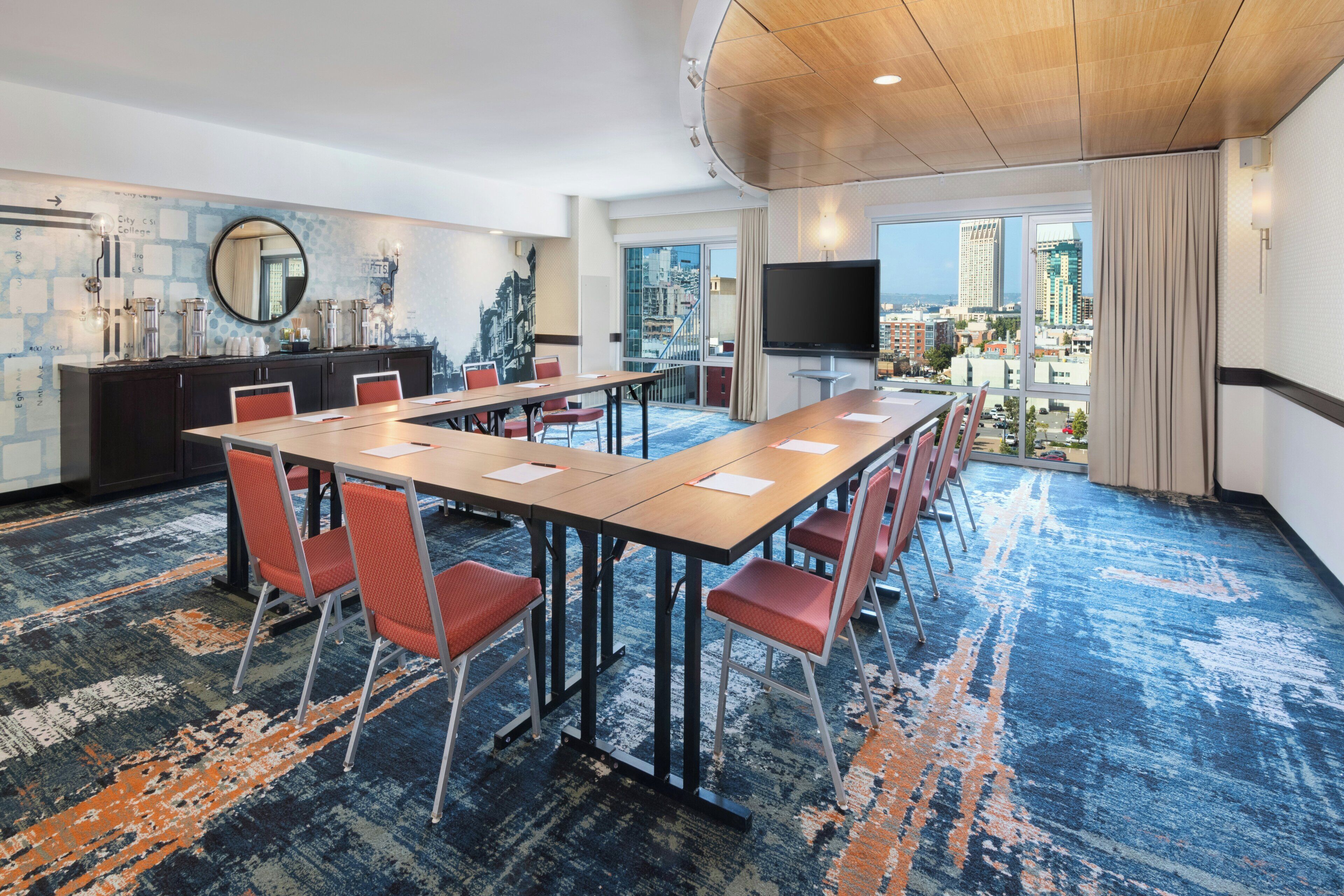 Une salle de conférence avec une longue table, des chaises, un téléviseur et une vue sur la ville.