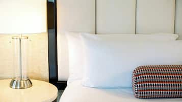 Una cama bien hecha con sábanas blancas y un cojín estampado, una mesita de noche redonda con una lámpara, y una pared con diseño de paneles verticales.