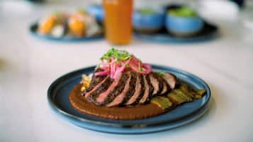 A plate of sliced steak with a sauce and garnish, a glass of beer, and other dishes in the background.