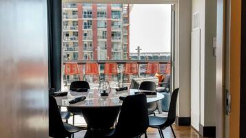 Een eethoek met een tafel en stoelen, uitzicht op een gebouw met balkons en een raam met uitzicht op de stadszicht.