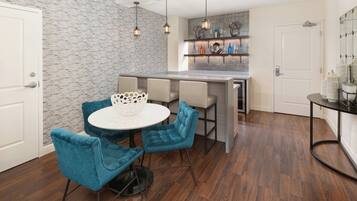 Una cocina moderna con una isla integrada, una zona de comedor con una mesa redonda y sillas azules, y una pared con estampado de ladrillo.