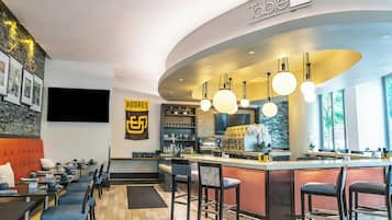 A modern bar area with a curved counter, hanging spherical pendant lights, and a large flat-screen TV mounted on the wall.