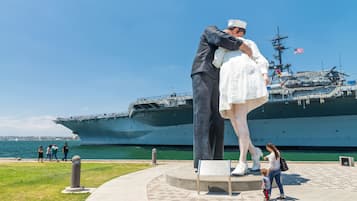 A naval ship docked at a port with a statue of a sailor and a child in the foreground.
