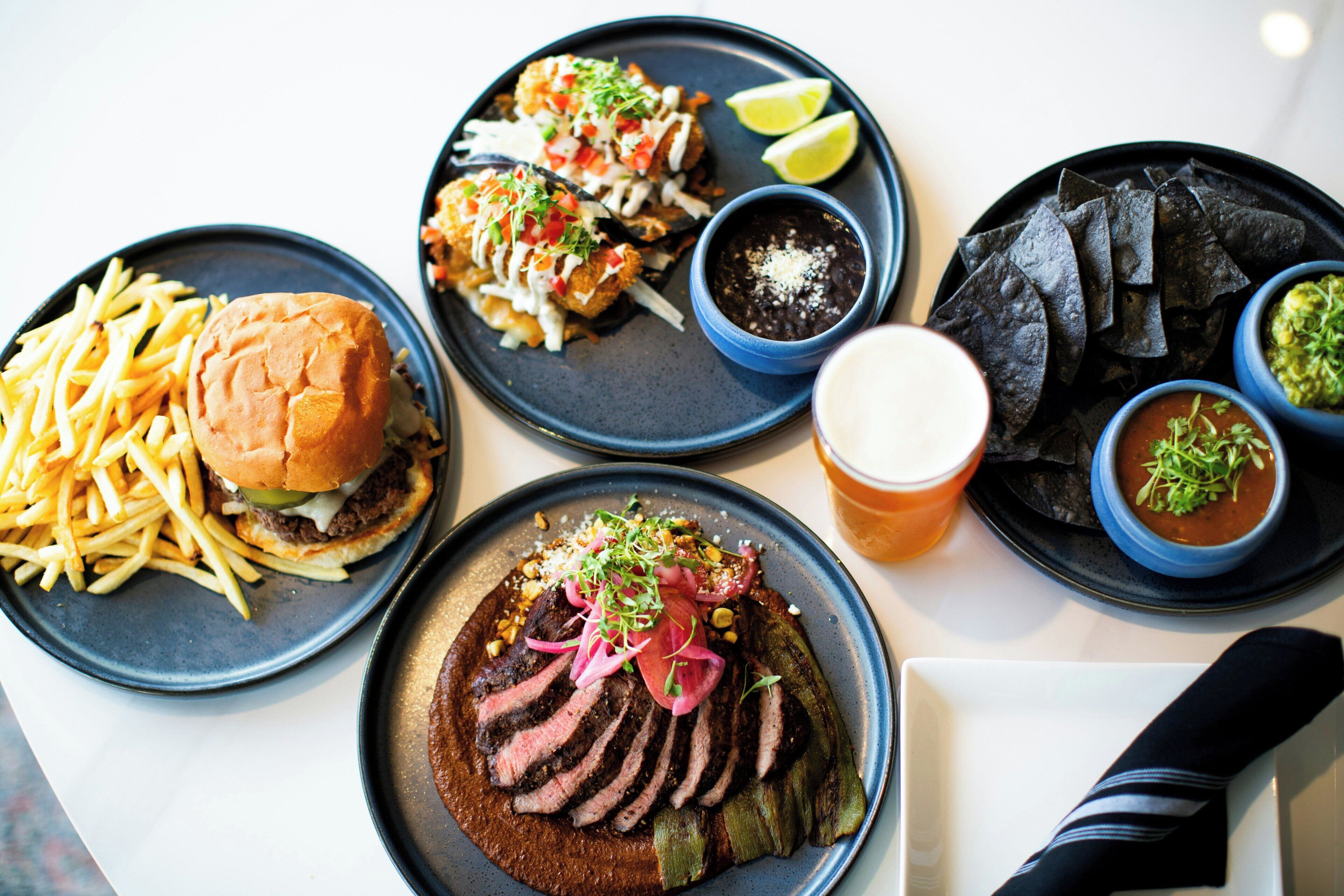 A variety of dishes including a burger, fries, tacos, and a steak dish, suggesting a diverse menu.