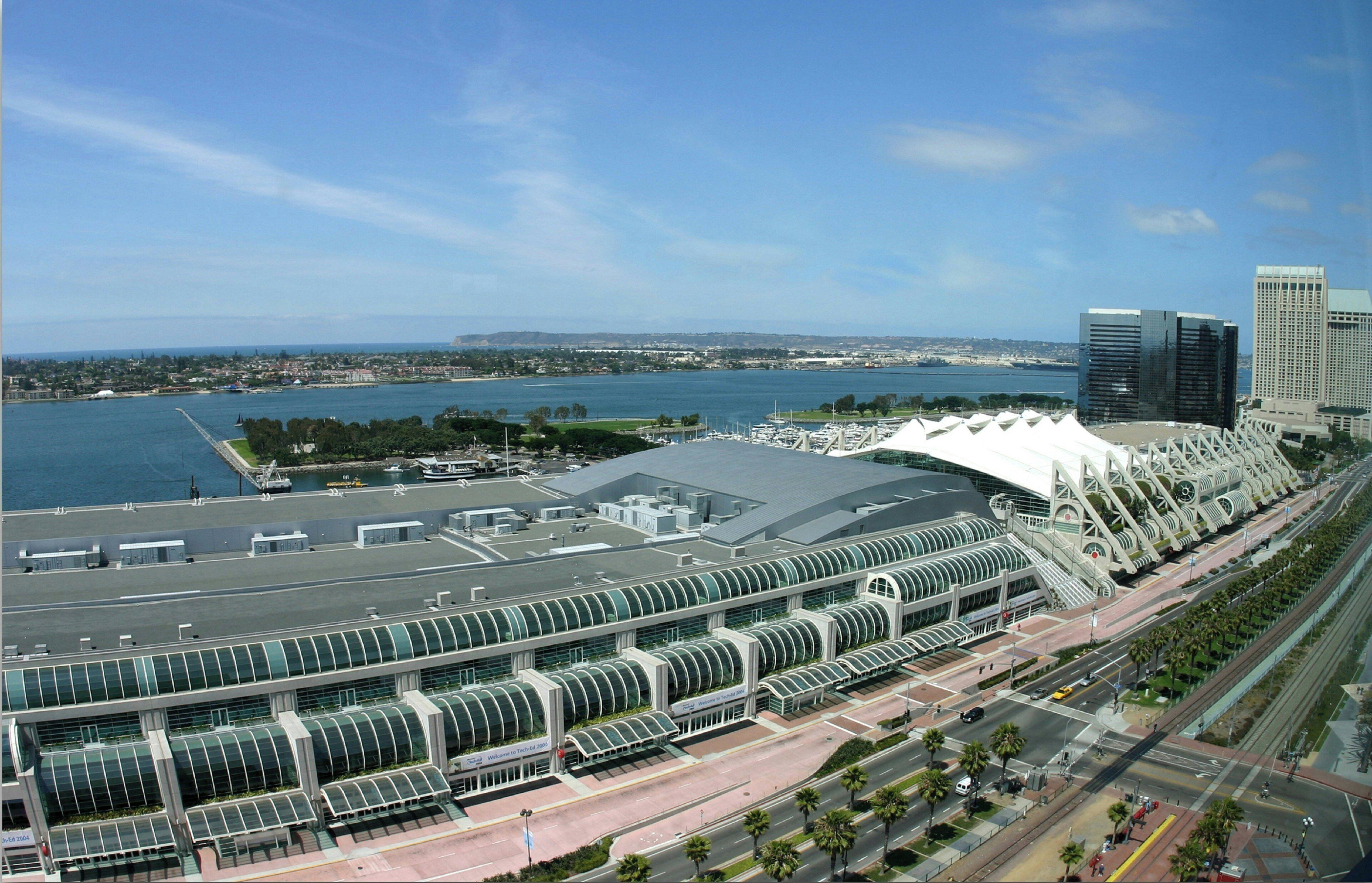 A modern building with a curved roof and a glass facade, adjacent to a body of water and a highway.