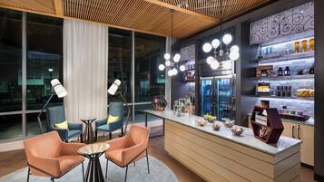 A modern bar area with seating, a refrigerator stocked with beverages, and a decorative wall.