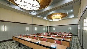 A conference room with long tables, red chairs, and a patterned carpet.