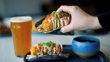 A hand holding a food item with a side of beer and a bowl.