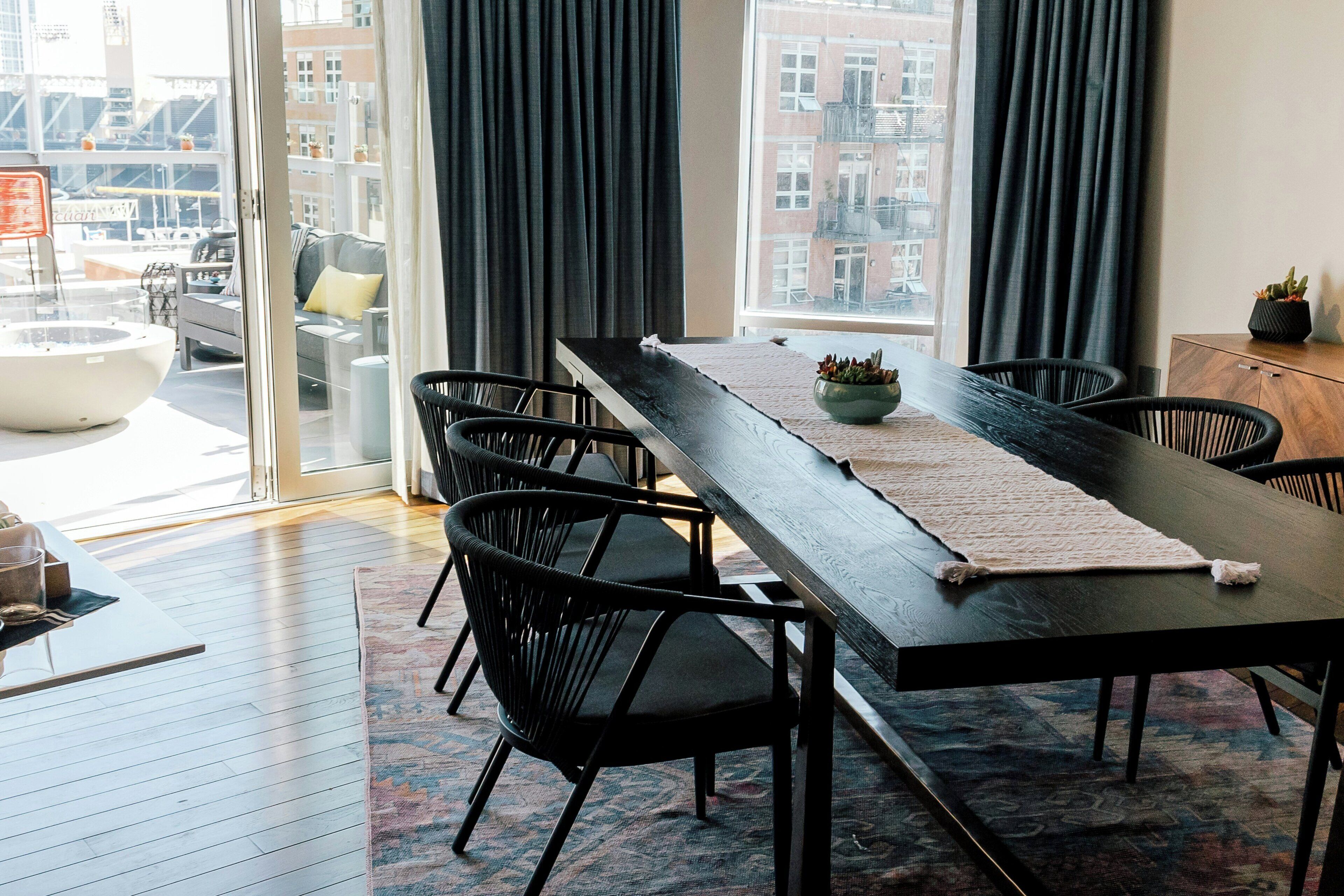 A modern dining area with a long table, black chairs, and a view of the city through large windows.
