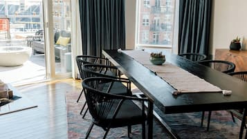 A modern dining area with a long table, black chairs, and a view of the city through large windows.