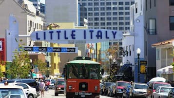 Escena callejera con un autobús que dice 'Old Town Trolley' y un cartel con la leyenda 'Little Italy' arriba.