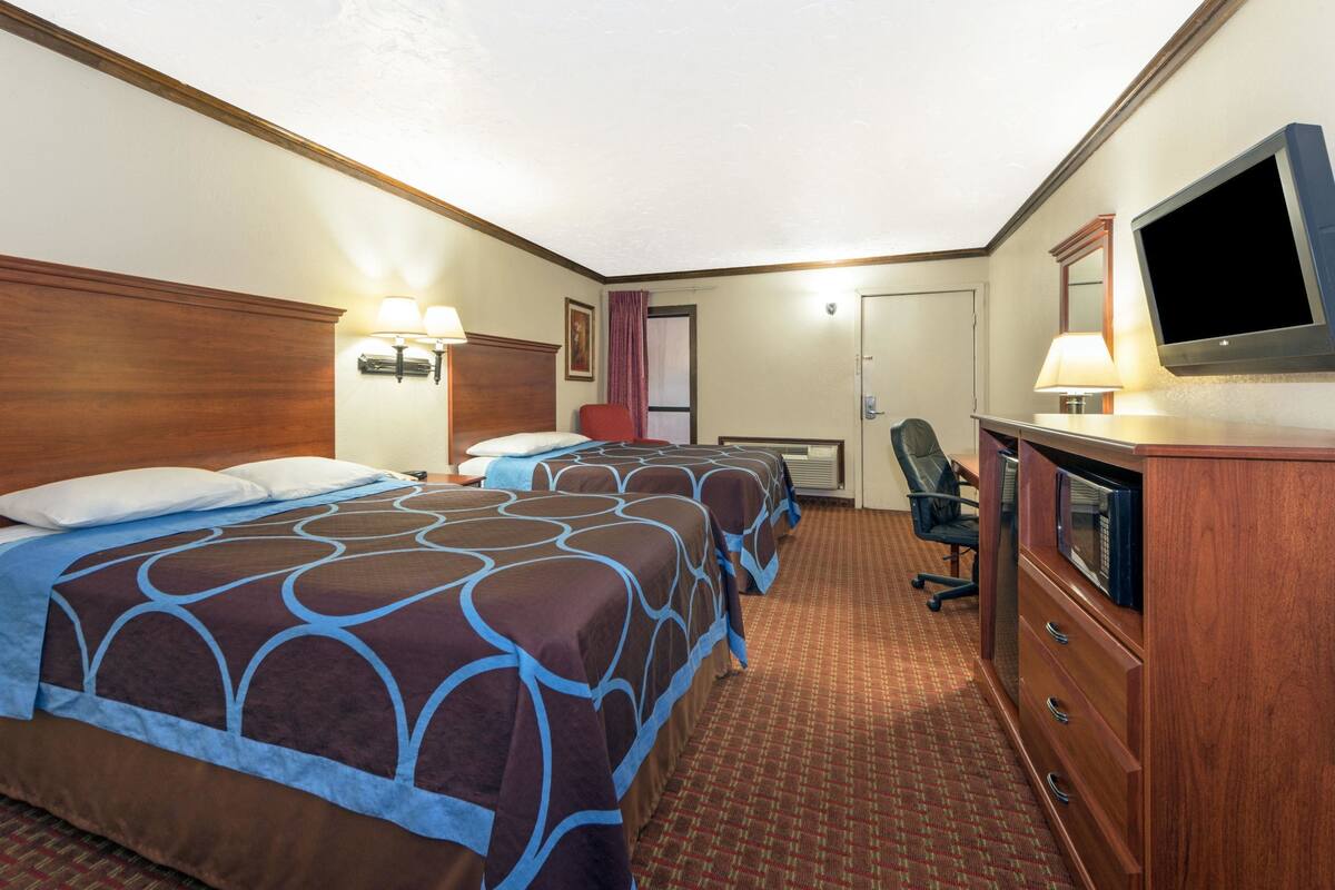 A hotel room with two beds, a desk, a chair, a television, and a wardrobe.
