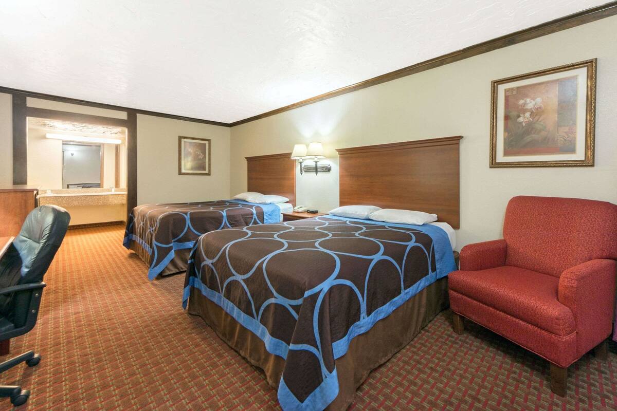 A hotel room with two beds, a desk, a chair, and a nightstand.