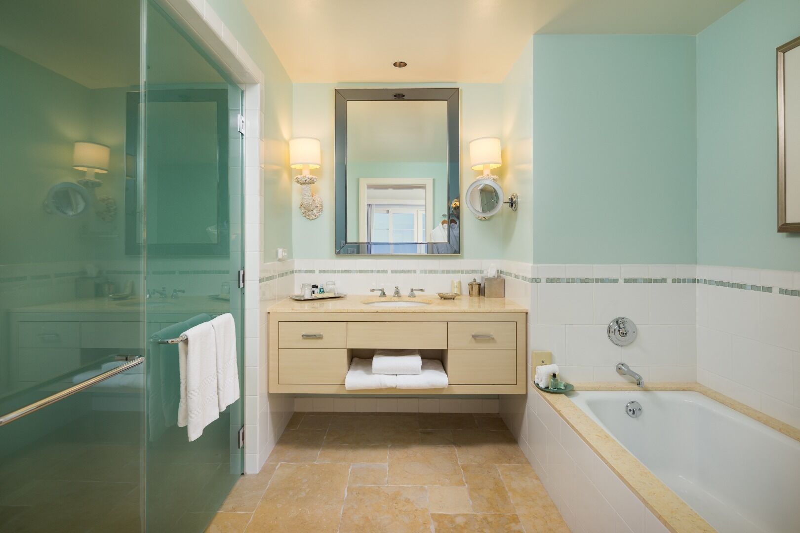 Un baño con cabina de ducha de vidrio, tocador color beige con espejo y una bañera.