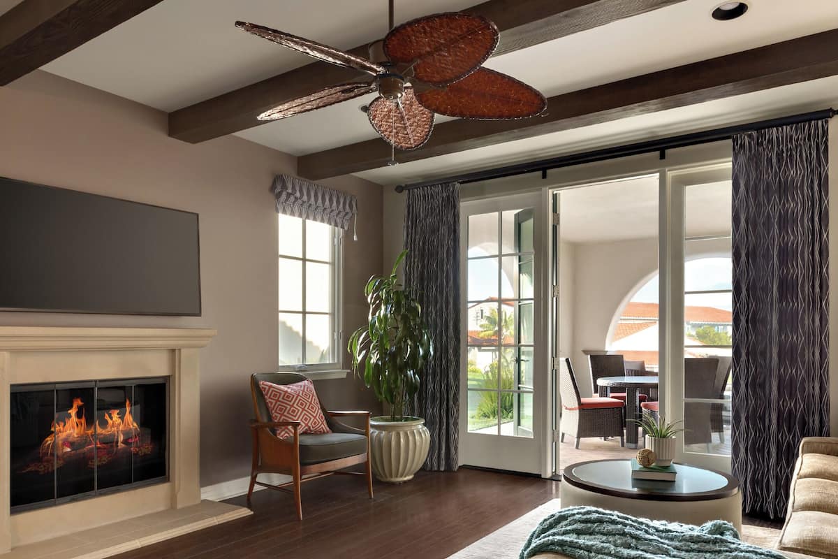 Una sala de estar con chimenea, ventilador de techo, comedor con asientos exteriores y un ventanal grande.