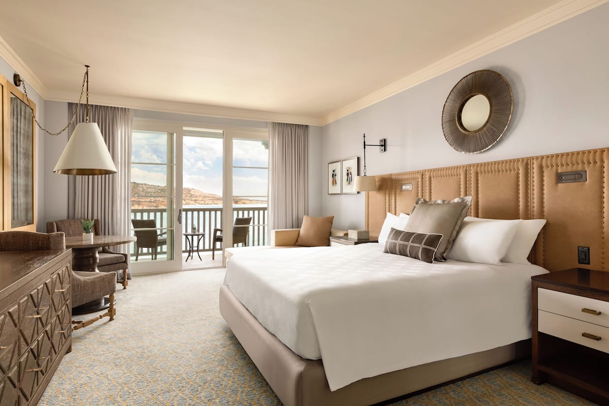 Habitación de hotel con una cama grande, un escritorio, una silla y un balcón con vistas.