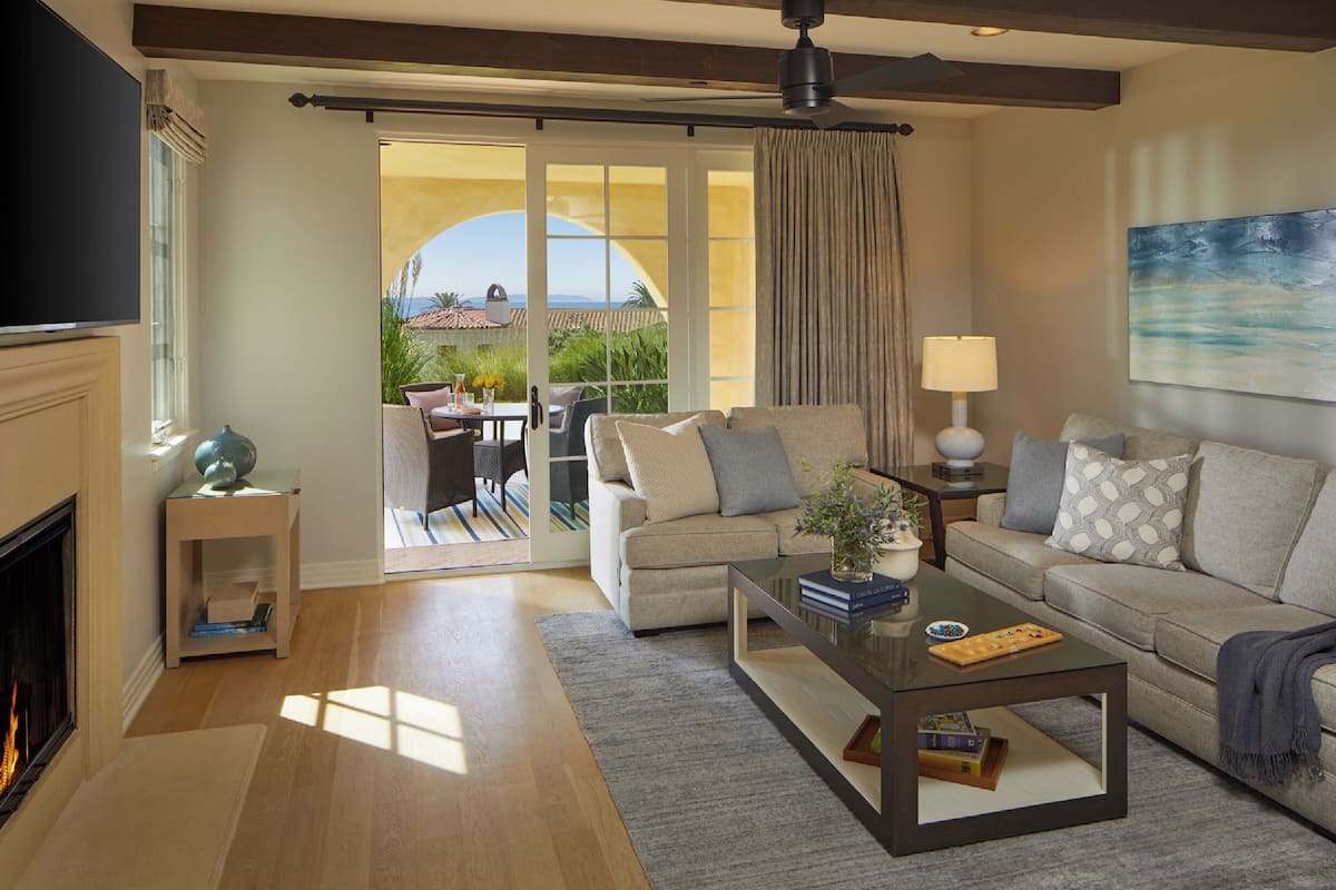 A spacious living room with a fireplace, a sofa, a coffee table, and a view of a patio with outdoor furniture.