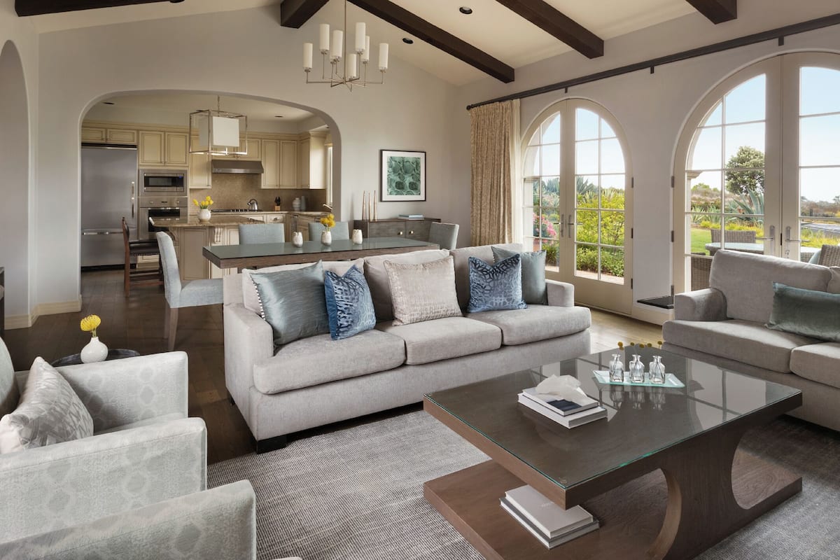 A spacious living room with a grey sofa, a glass coffee table, and a view of the kitchen and outdoor patio.