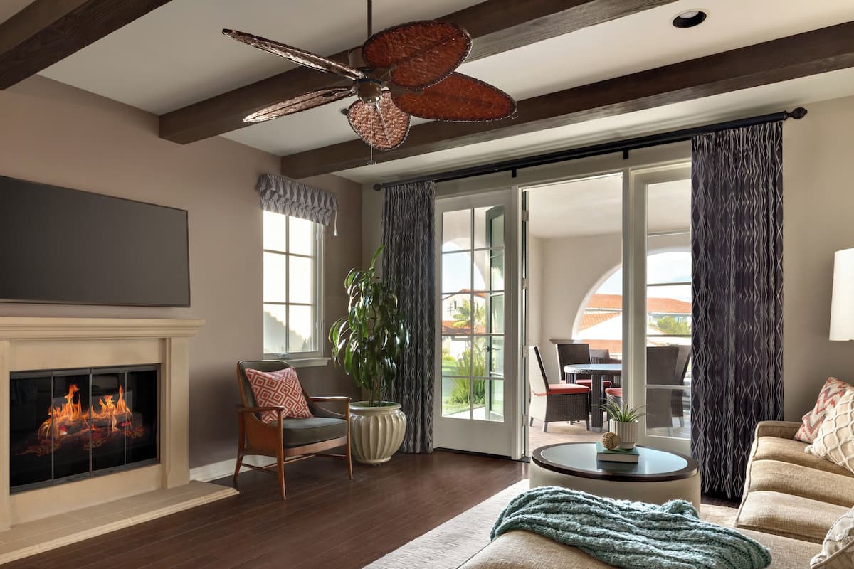 A living room with a fireplace, a ceiling fan, a large window, and a sliding glass door leading to an outdoor patio.