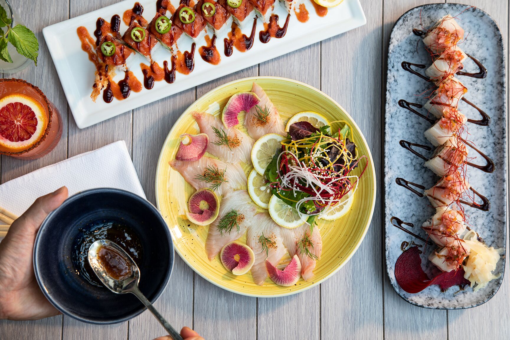 Variedad de piezas de sushi en diferentes platos, un vaso de bebida y un tazón de salsa.