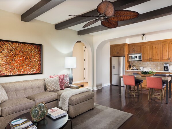 A modern living room with a sectional sofa, a coffee table with books, and a dining area with a kitchen in the background.