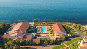 Vista aérea de un resort con piscina, varias edificaciones y una costa.