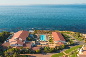 Vista aérea de un resort con piscina, varias edificaciones y una costa.