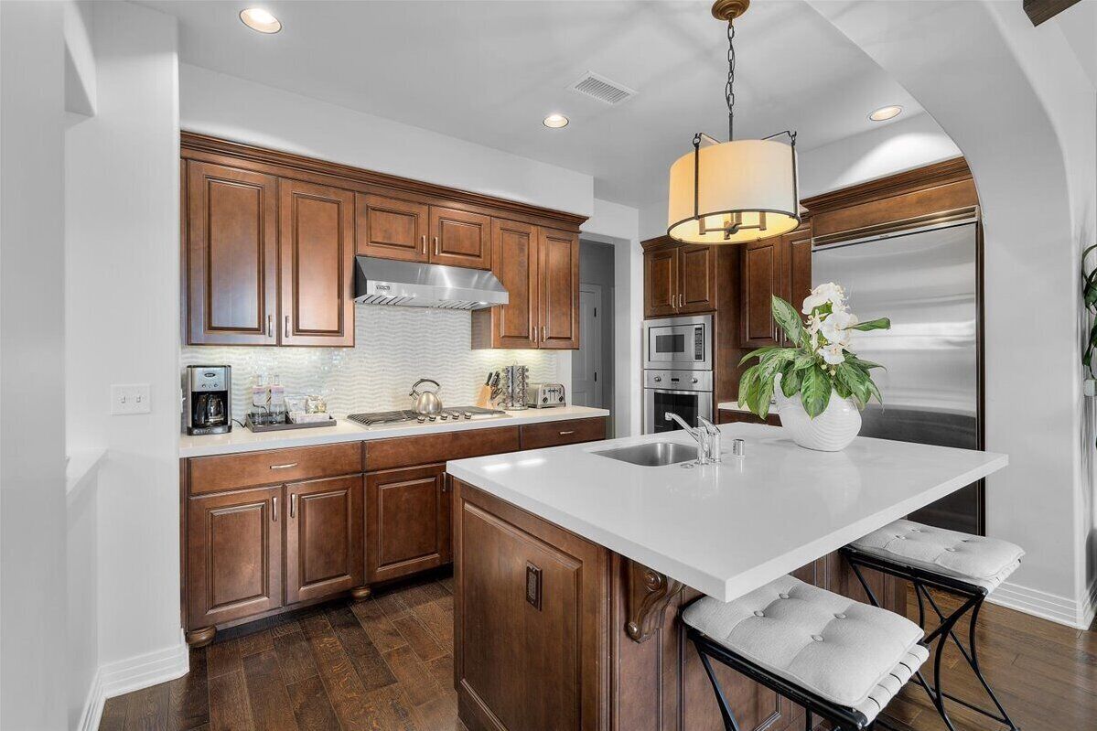 Una cocina moderna con armarios de madera, una isla grande, electrodomésticos de acero inoxidable y una lámpara colgante.