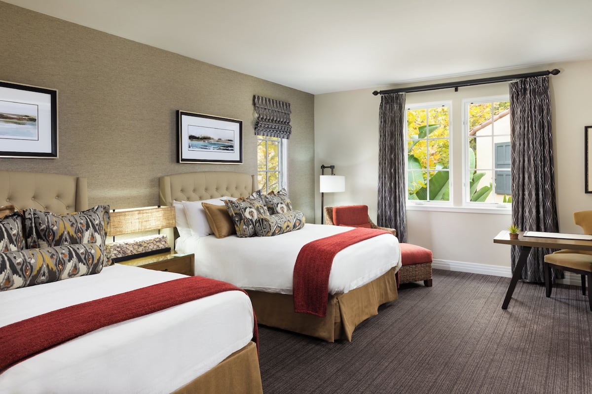 A hotel room with two beds, a desk, and a chair.
