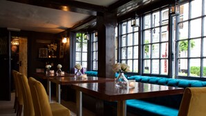 A restaurant with a long wooden table, yellow chairs, teal cushioned seating, and large windows with a view of the outside. - The Talbot Inn (Woking)