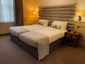 A hotel room with two beds, a wooden nightstand, and a large headboard.