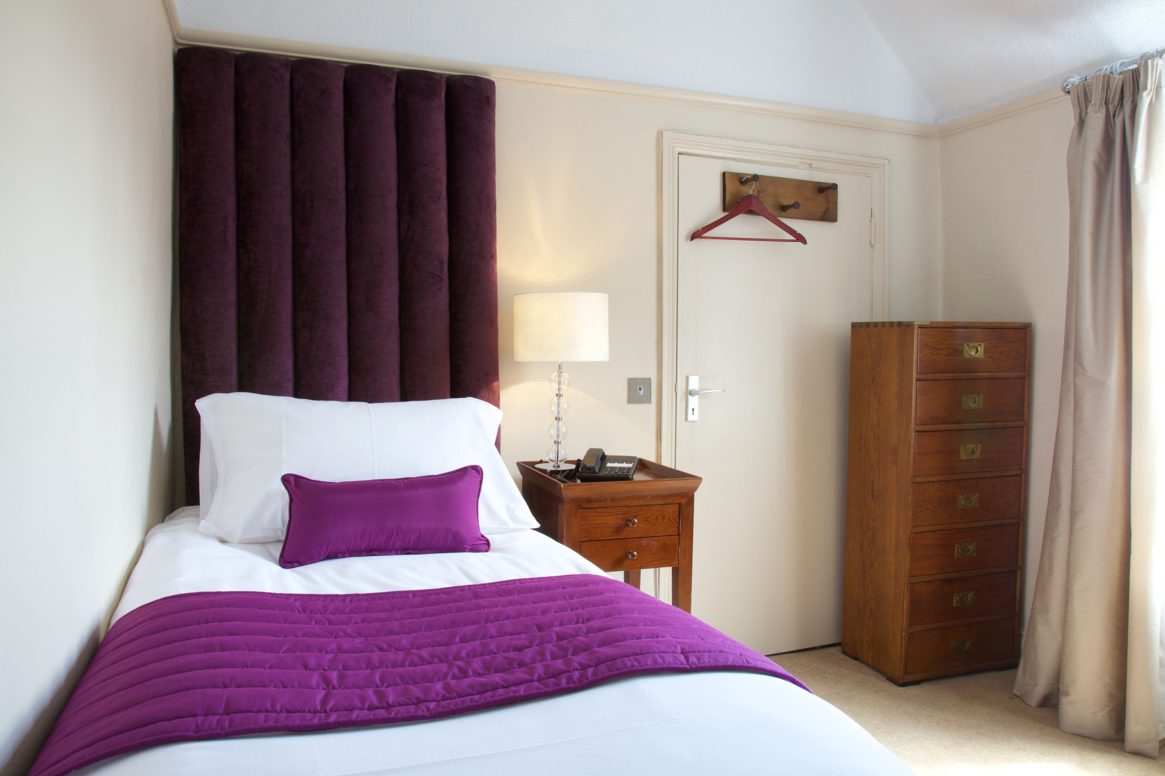 Un dormitorio con cama, mesita de noche, cómoda y una puerta con perchero.