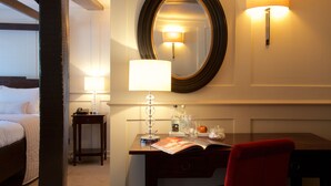 A hotel room with a bed, a desk with a lamp, a mirror, and a red chair. - The Talbot Inn (Woking)