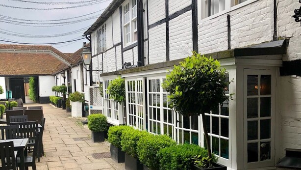 A traditional building with white walls and black timber framing, featuring a row of black planters with green shrubs along the side. - The Talbot Inn (Woking)