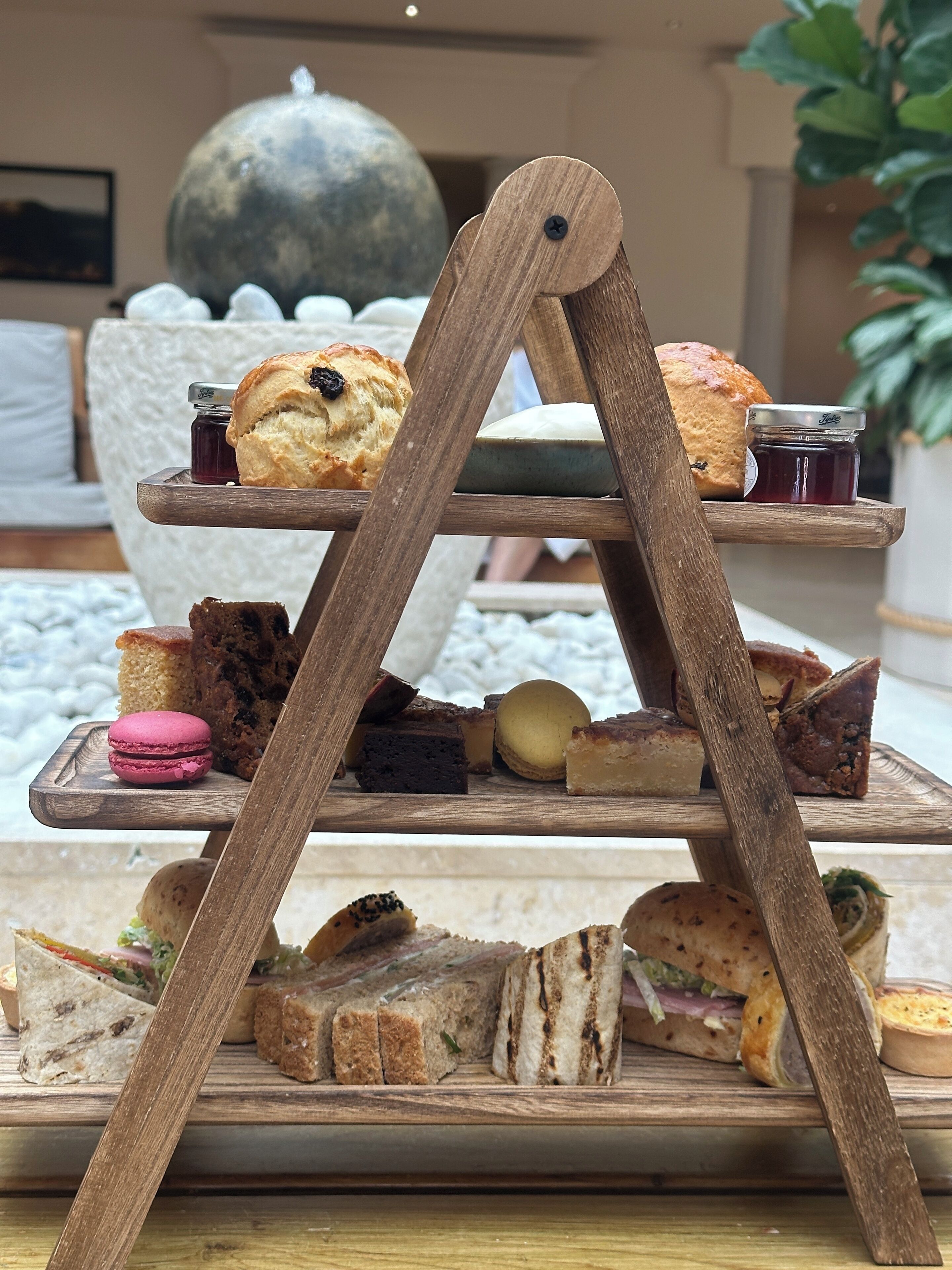 Una bandeja de madera escalonada con diversos pasteles, sándwiches y macarons.