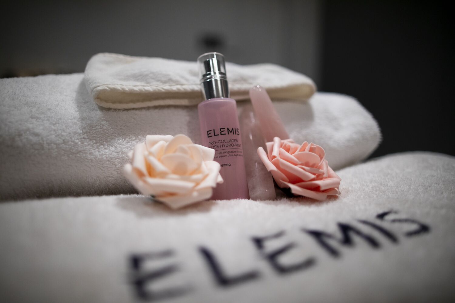 Een handdoek met de naam "ELEMIS" en twee roosvormige decoraties.