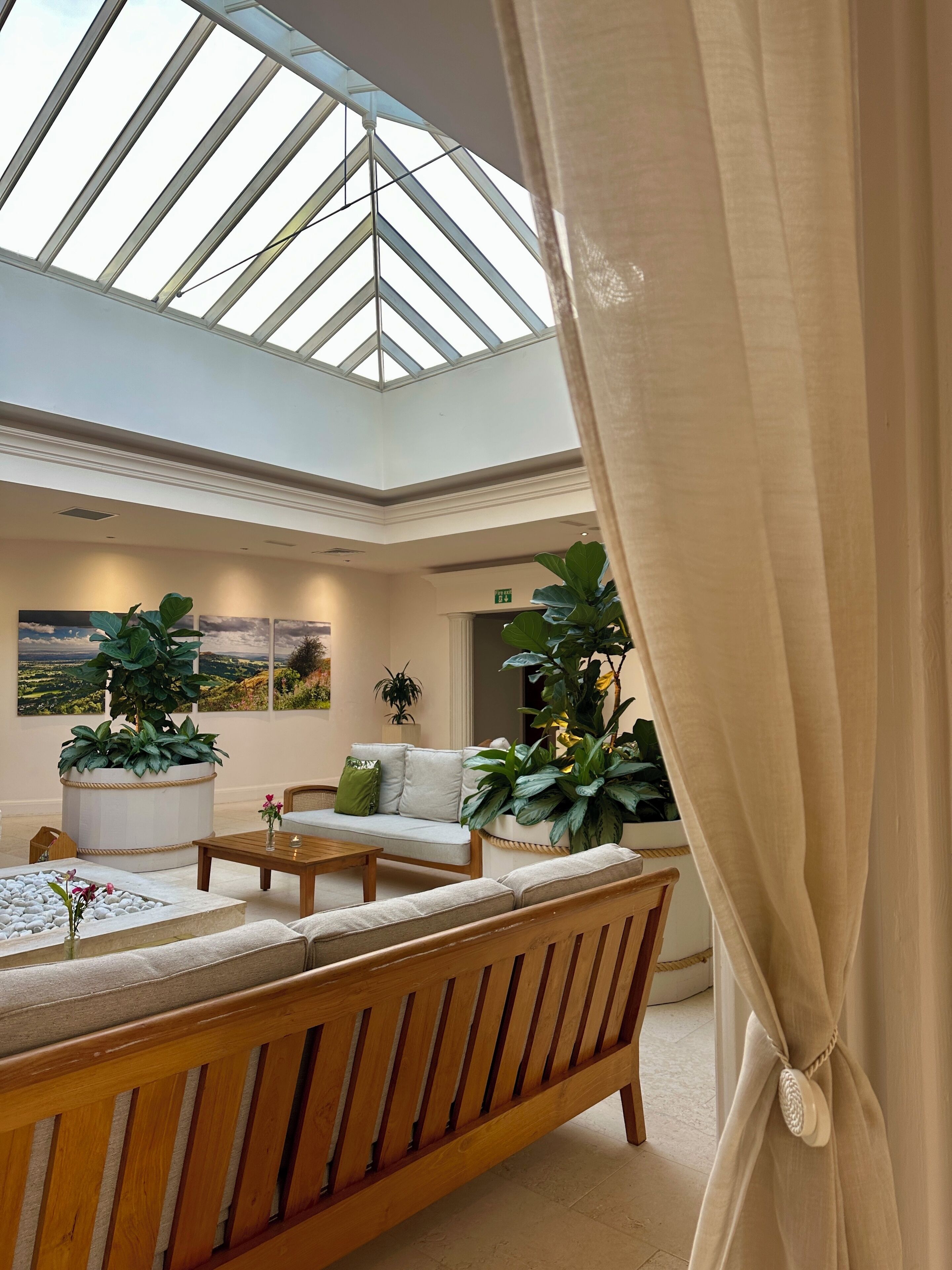 A spacious interior with a high ceiling and skylight, featuring a wooden bench, a sofa, and potted plants.